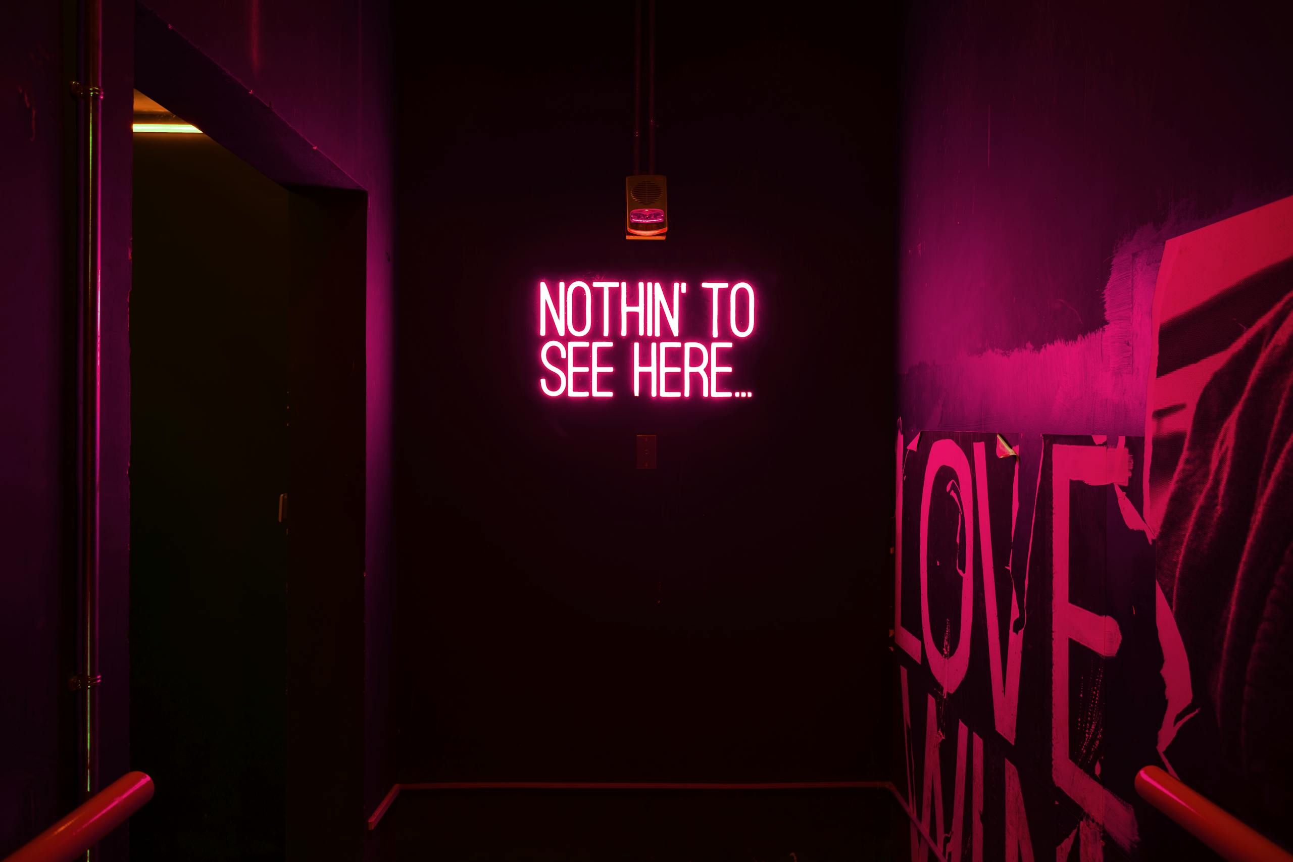 Neon sign reading 'Nothin' to see here...' in an artistic dark room.